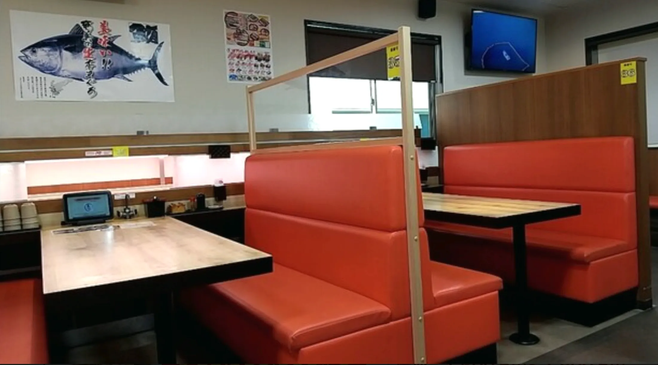オレンジのボックス席が並ぶ店内。壁に本まぐろのポスターが貼られ、各席に注文用のタッチパネルが置かれている