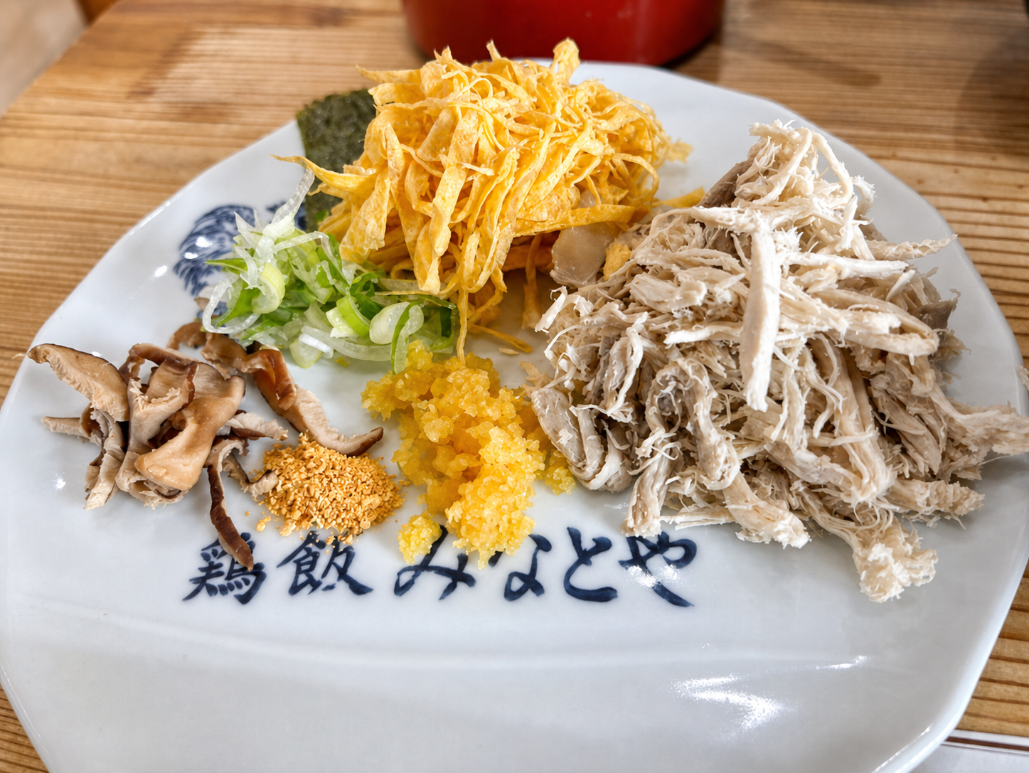 鶏飯みなとやと書かれた皿に盛られた、鶏のほぐし身や錦糸卵などの具材